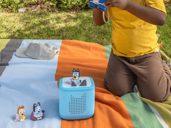 child playing with a blue toniebox 2 and three Bluey Tonies outside