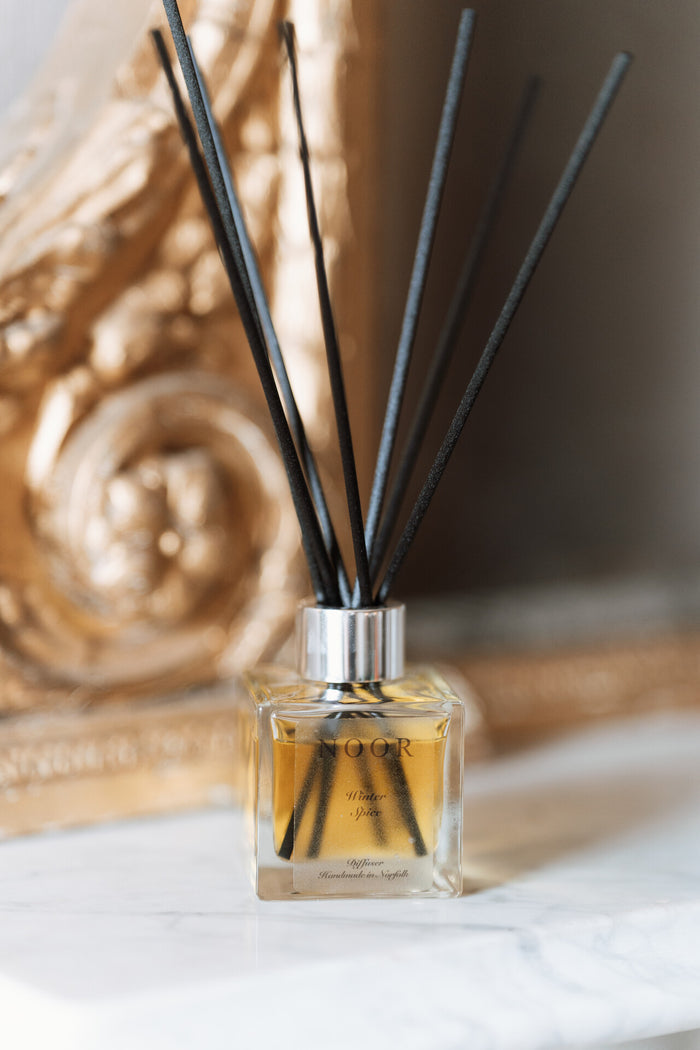Reed diffuser with black reeds in a decorative glass bottle on a marble surface.