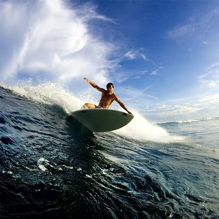 Surfer riding a large wave, capturing action footage with an action camera mounted for a first-person POV.