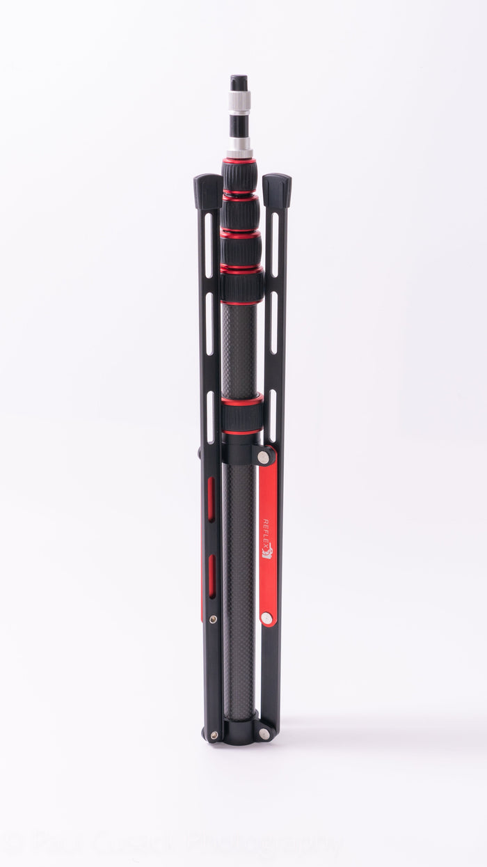 Folded black and red carbon fiber tripod with twist locks, standing upright on a white background, showing the Reflex Camera logo.