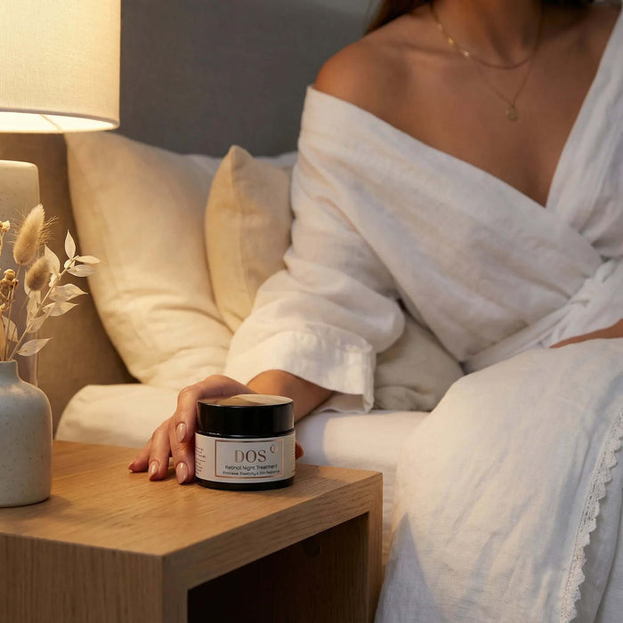 Retinol night cream jar on wooden bedside table next to lamp and woman in comfortable robe. DOS Cosmetics